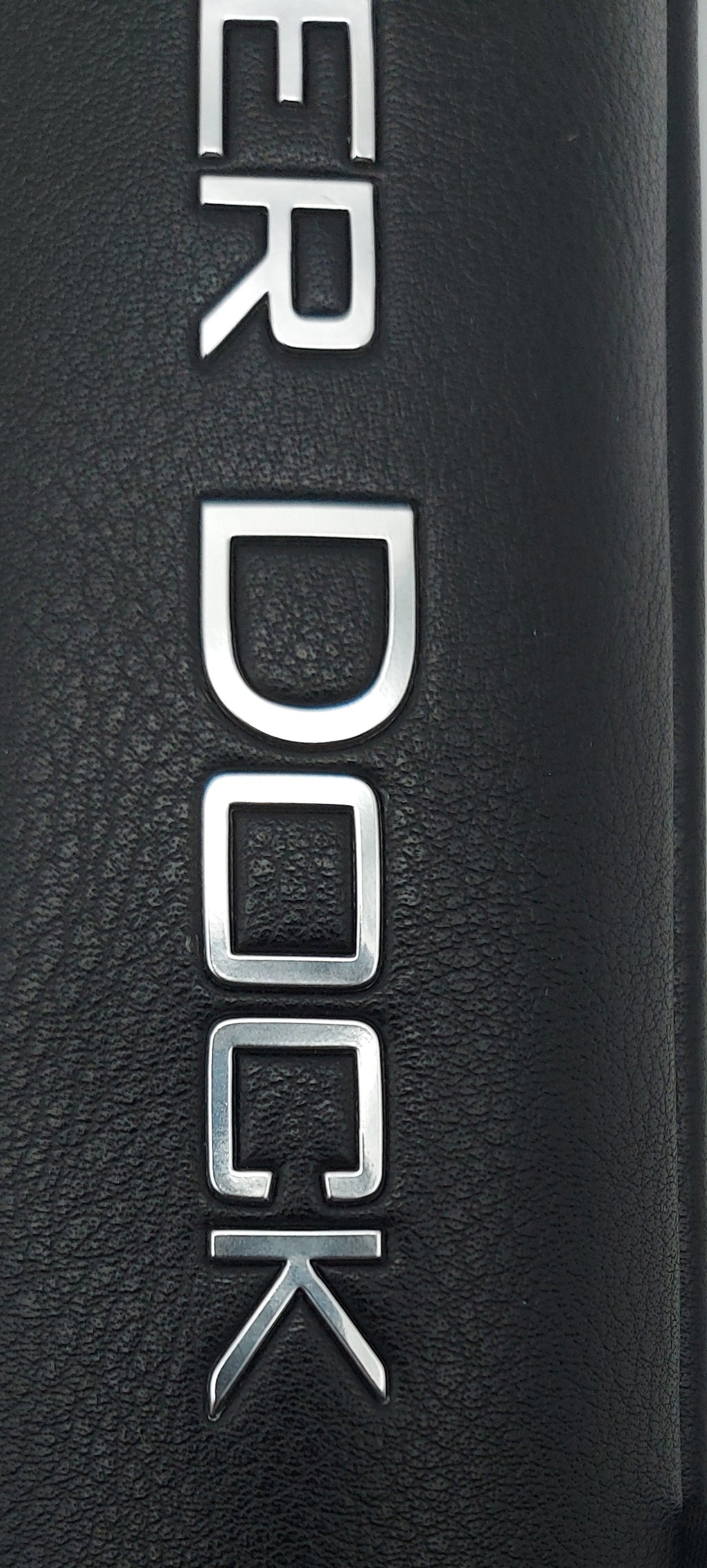 Close-up of a black textured cylindrical product, likely a golf bag or case, with silver 'COVER DOCK' lettering and a small black brand tag reading 'COVER DOCK GOLF'.