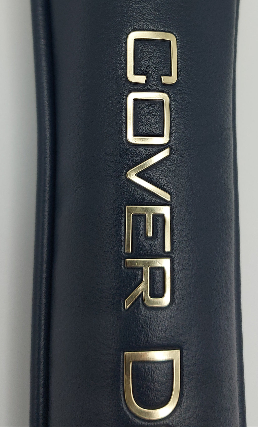 Close-up of a dark navy blue textured leather or faux-leather cylindrical item with large metallic gold 'COVERD' lettering printed vertically on the side.