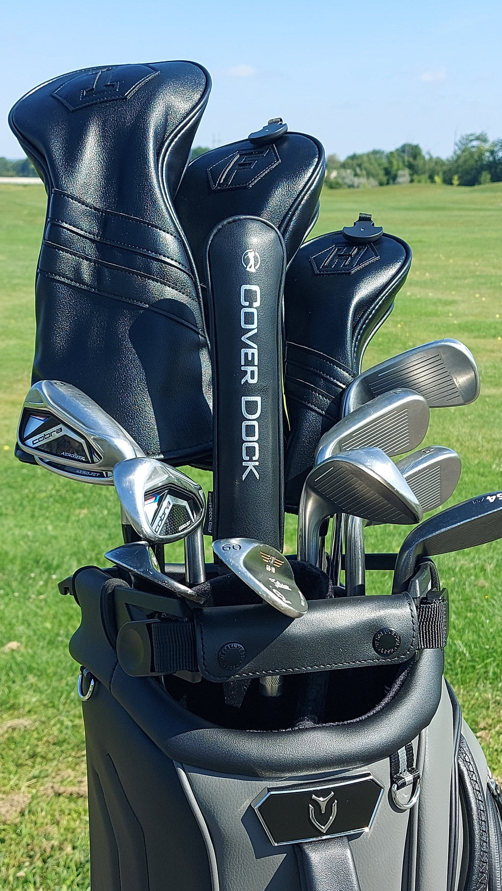 A golf bag on a grassy golf course with several black and silver golf clubs inserted. The bag is branded Callaway, and the club headcovers are branded Cover Dock.