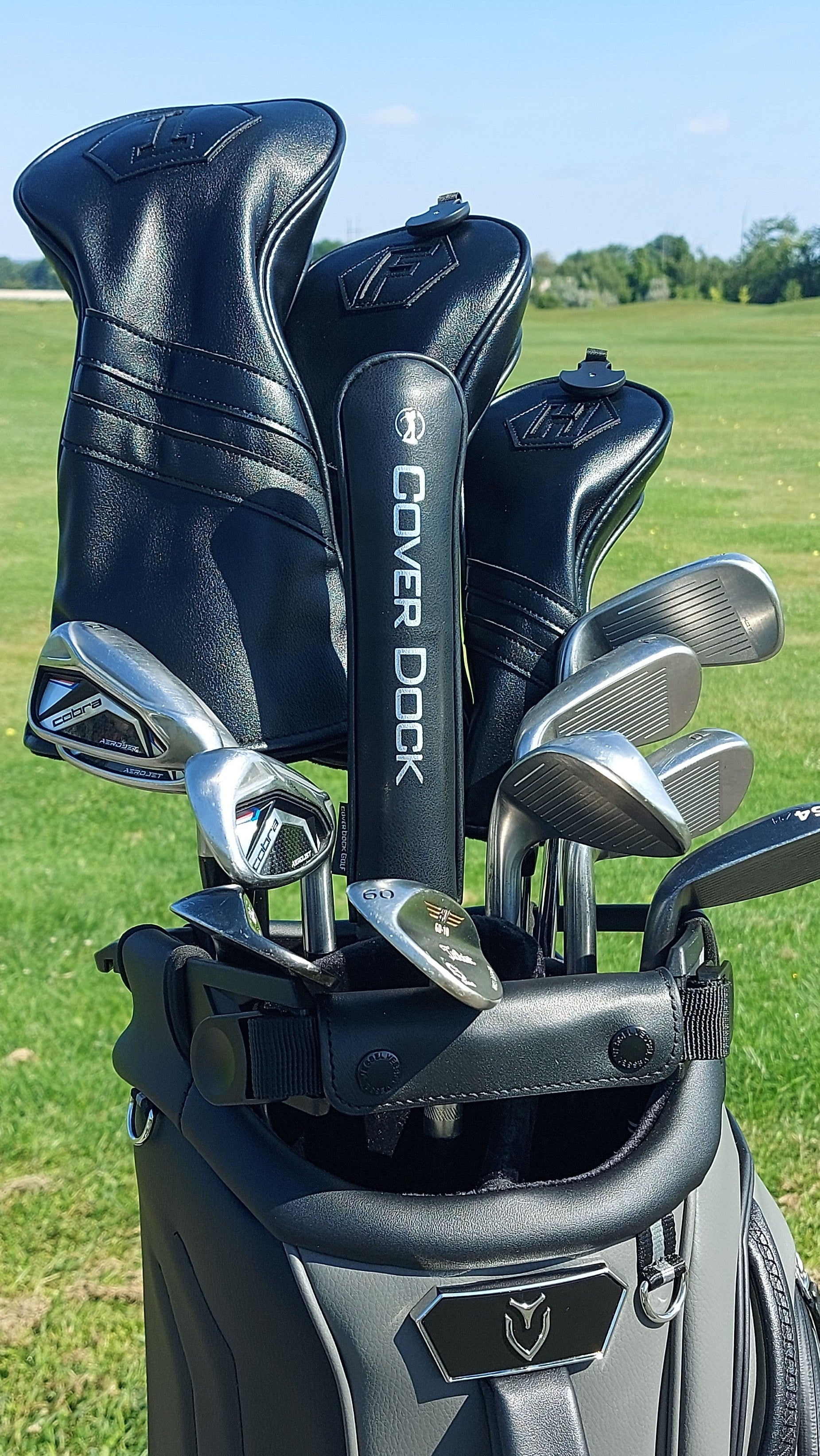 A golf bag on a grassy golf course with several black and silver golf clubs inserted. The bag is branded Callaway, and the club headcovers are branded Cover Dock.
