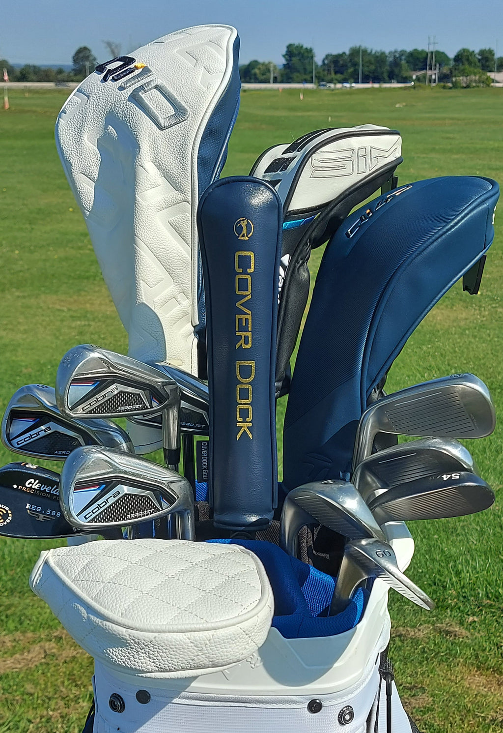A golf club bag filled with golf clubs and fitted clubheads on an outdoor grassy golf course. Visible brands include Cover Dock on the central neck cover and Callaway on the clubheads.
