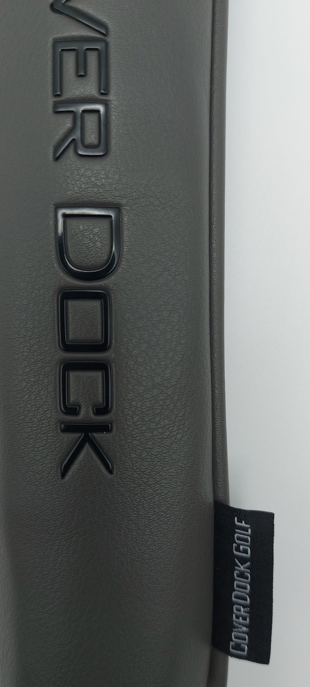 Close-up of a dark gray textured leather or faux-leather surface with embossed 'COVER DOCK' lettering and a small black fabric tag reading 'COVER DOCK GOLF'.