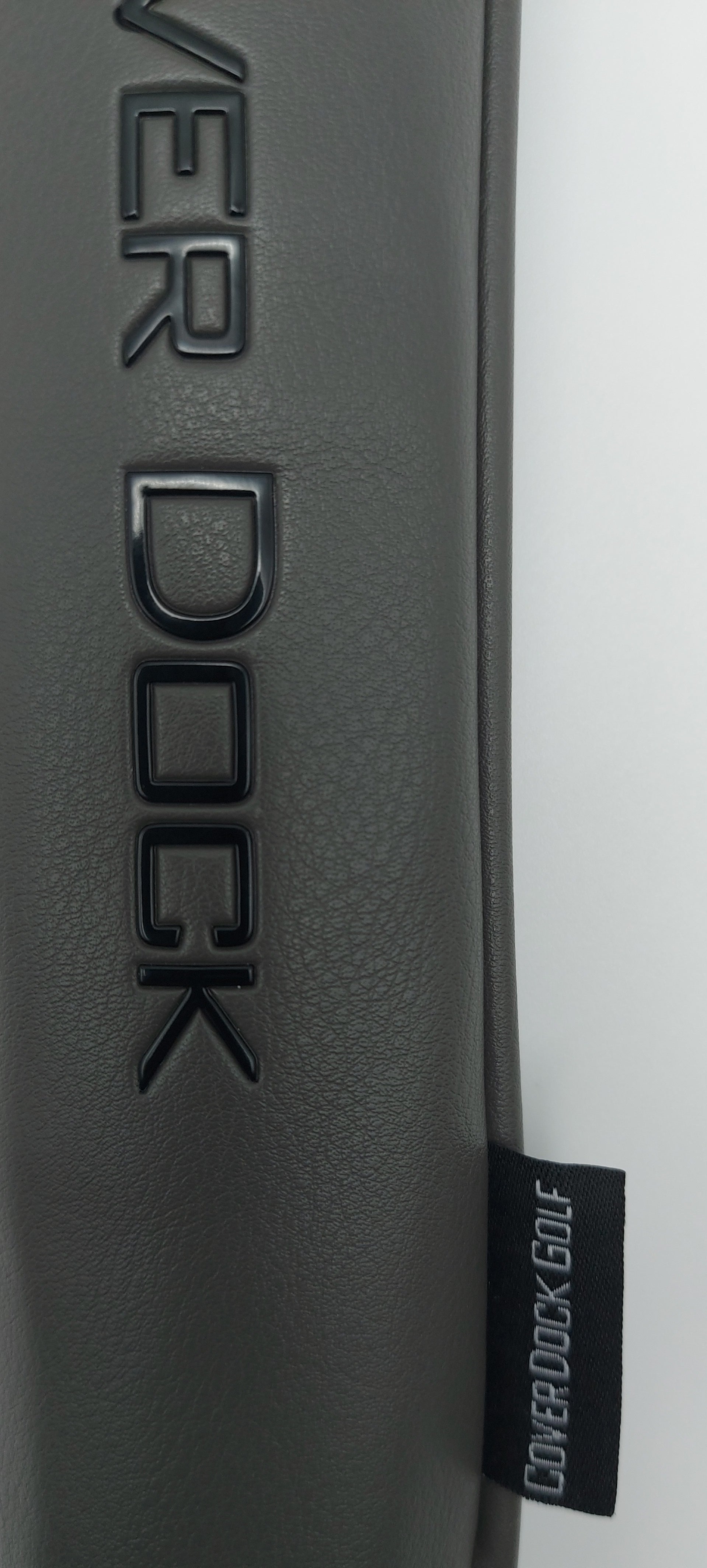 Close-up of a dark gray textured leather or faux-leather surface with embossed 'COVER DOCK' lettering and a small black fabric tag reading 'COVER DOCK GOLF'.