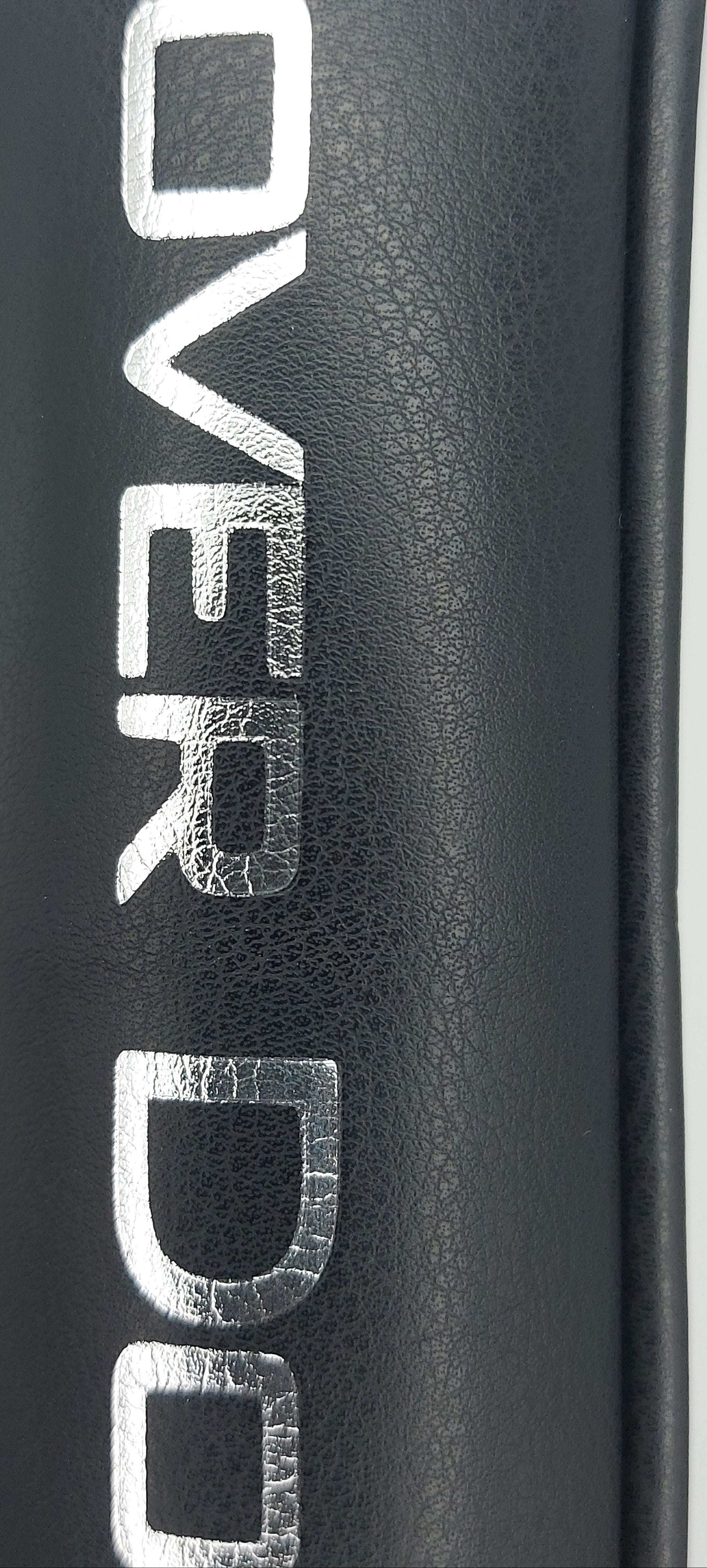 Close-up of a black vegan leather surface with silver metallic lettering that appears to read 'COVER DO'.