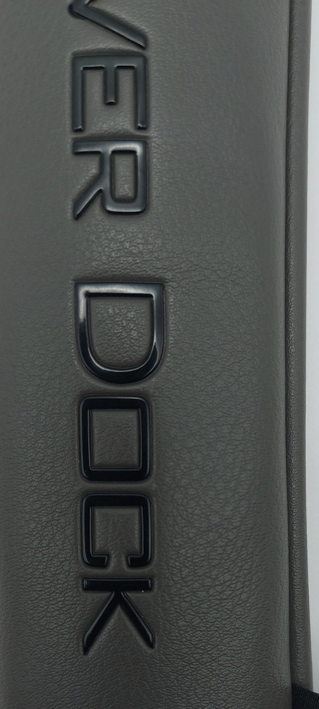 Close-up of a dark gray textured leather or faux-leather surface with embossed 'COVER DOCK' lettering and a small black fabric tag reading 'COVER DOCK GOLF'.
