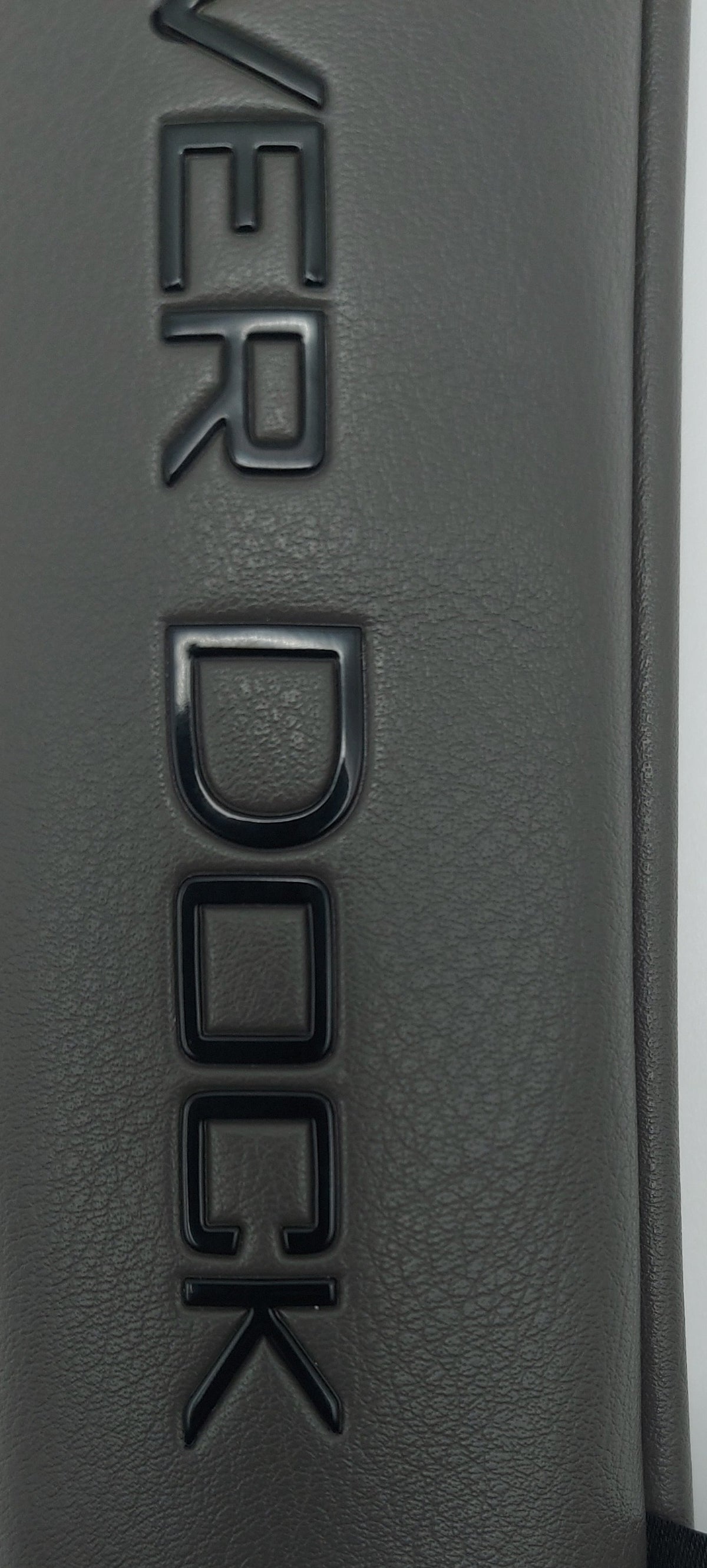 Close-up of a dark gray textured leather or faux-leather surface with embossed 'COVER DOCK' lettering and a small black fabric tag reading 'COVER DOCK GOLF'.