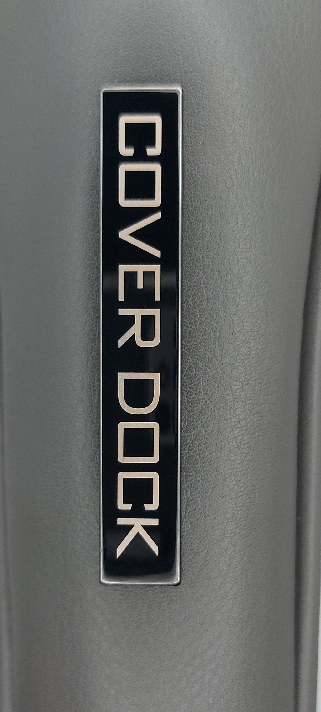 Close-up of a dark gray textured product surface with a black rectangular badge reading 'COVER DOCK' in light lettering.