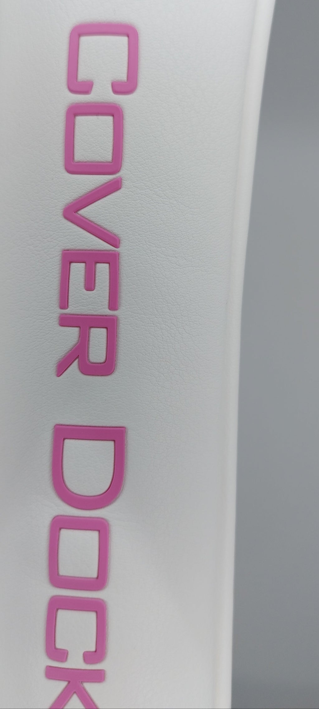 Close-up of a white curved surface with pink raised lettering reading 'COVER DOCK' against a gray background.