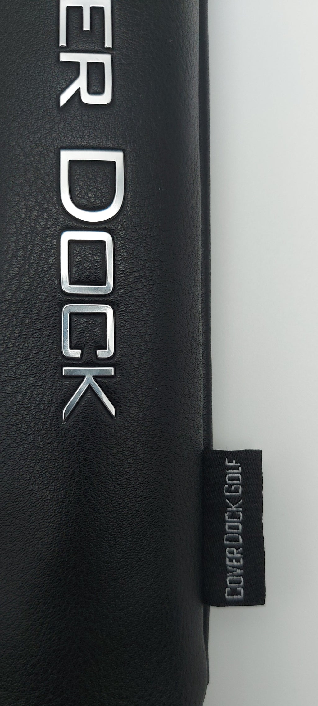 Close-up of a black textured cylindrical product, likely a golf bag or golf club head cover holder for a bag, with silver 'COVER DOCK' lettering and a small black brand tag reading 'COVER DOCK GOLF'.