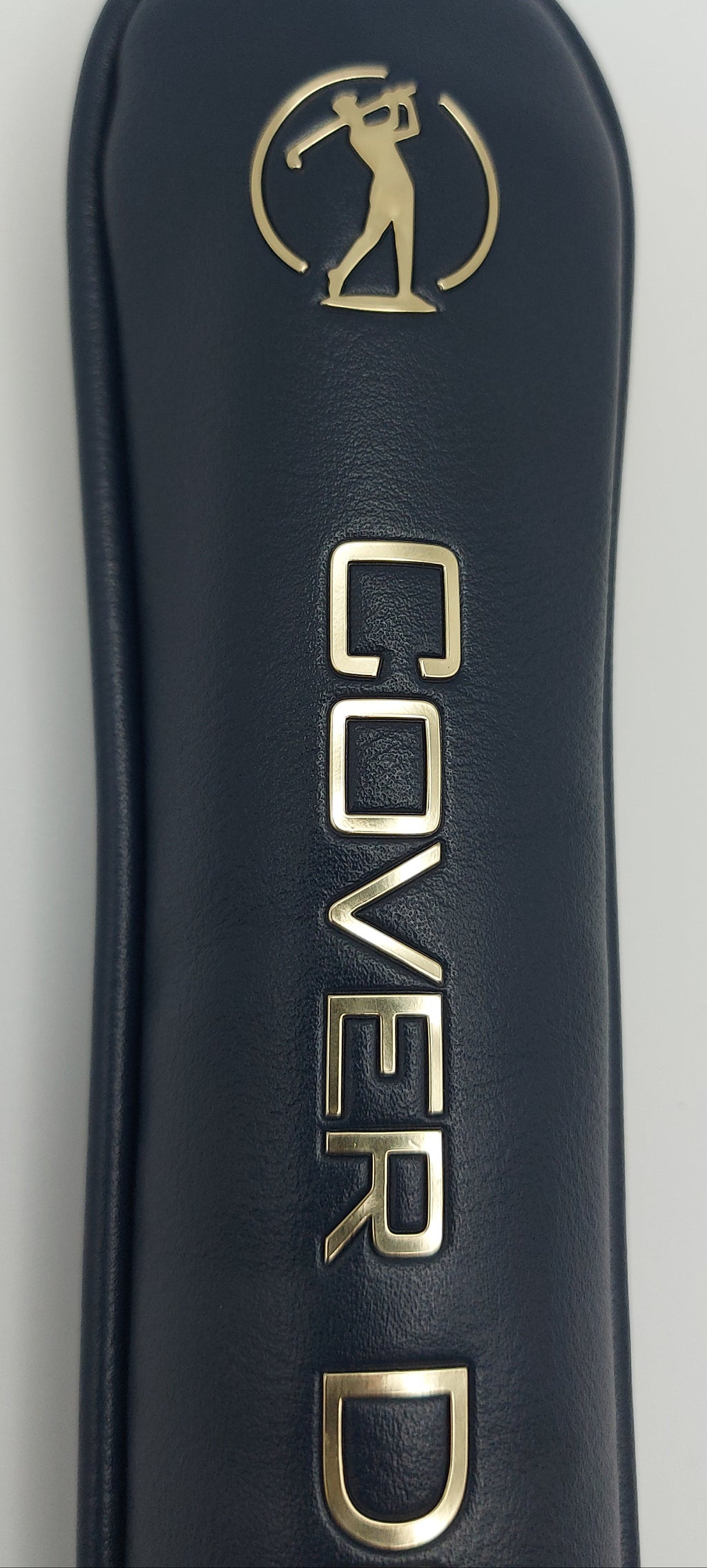 Close-up of a nay blue golf club cover with gold lettering reading 'COVER D' and a gold golfer decal near the top, shown against a light neutral background.
