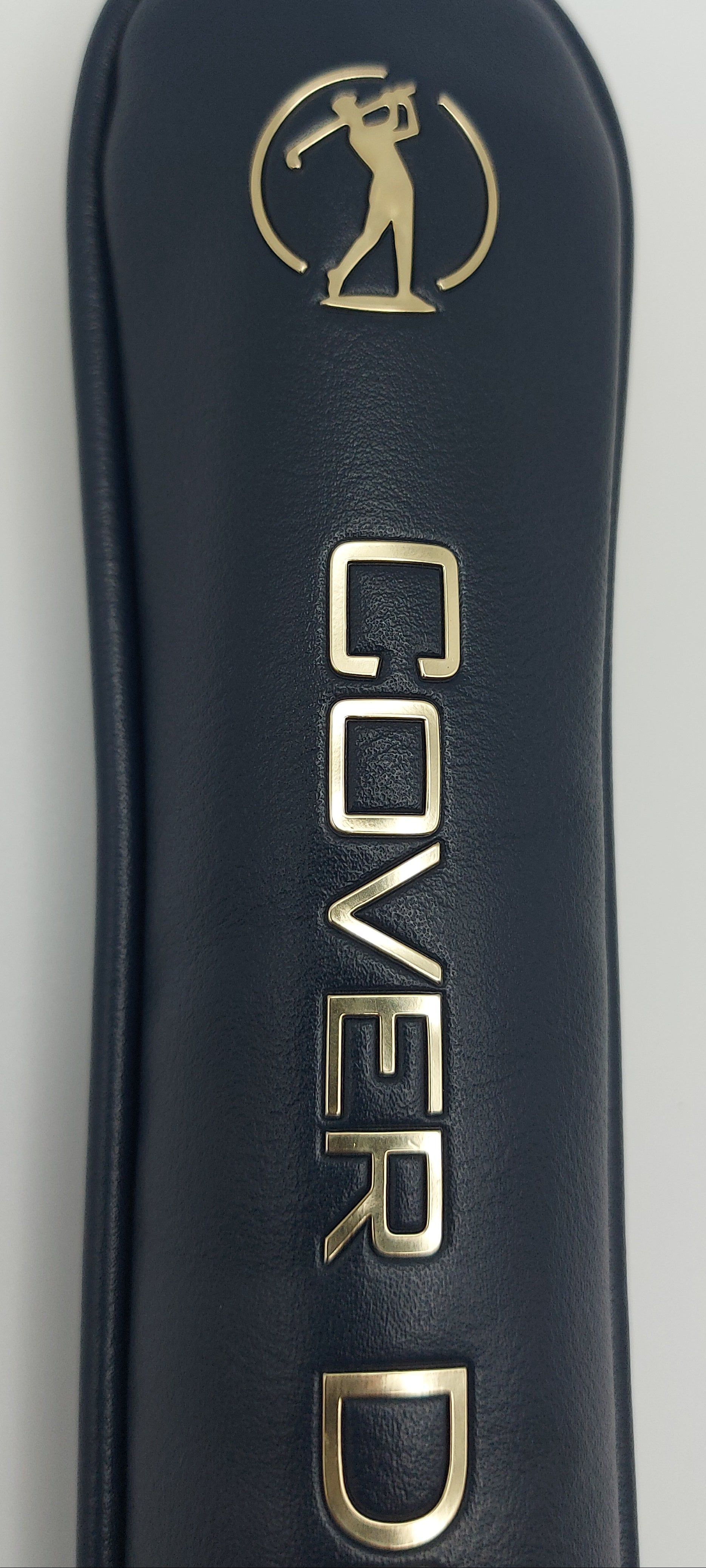 Close-up of a nay blue golf club cover with gold lettering reading 'COVER D' and a gold golfer decal near the top, shown against a light neutral background.